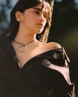 Collar con dije colgante de forma orgánica e irregular, acabado dorado, suspendido de un cordón negro de algodón natural.