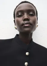 Chaqueta entallada de color negro con cuello mao y cierre frontal de botones dorados. Presenta un diseño estructurado de manga larga y forro interior.