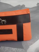 Sobre o cartuchera de lona fucsia con terminaciones y detalles de cuero marrón. Cuenta con cierre superior y aplique metálico de caballo en la parte frontal, además de una etiqueta de cuero con la marca grabada.