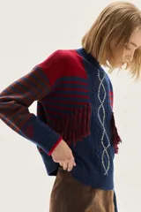 Polera de tejido de punto con diseño multicolor que combina rayas horizontales, trenzas verticales y flecos decorativos. Presenta cuello semi polera, mangas largas con bordado y puños acanalados.