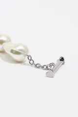 Collar asimétrico compuesto por una mitad de perlas de vidrio blancas y una mitad de cadena de eslabones plateados, con un dije de corazón negro en forma de candado y cierre de barra T.