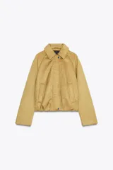 Chaqueta bomber de efecto ante en color tostado, con cuello solapa, manga larga y bolsillos laterales. Presenta un diseño con bajo acabado en pliegues que aporta volumen y cierre frontal con cremallera y botones a presión.