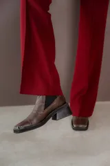 Botas tipo chelsea de cuero color marrón oscuro con acabado brillante. Presentan punta cuadrada con detalle de puntera metálica, elásticos laterales y taco cuadrado bajo.