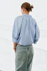 Camisa de algodón con cuello solapa, mangas abullonadas por debajo del codo y bajo acabado en globo. Presenta cierre frontal con botones ocultos.