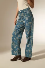 Pantalon de jean de corte recto con estampado floral en tonos claros sobre base azul. Presenta bolsillos funcionales y tiro medio.