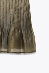 Blusa de manga corta con escote barco, confeccionada en tejido satinado color verde oliva. Presenta un diseño holgado en la parte superior y un canesú inferior con pliegues verticales ajustados.