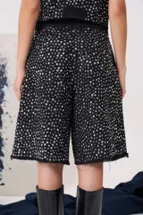 Bermuda de jean negro con tiro medio, largo a la rodilla y ruedo desflecado. Presenta un diseño cubierto de apliques metálicos plateados tipo tachas, con bolsillos funcionales.