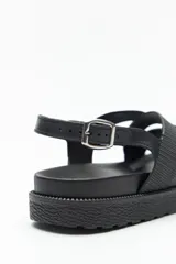 Sandalia negra con tiras entrelazadas ajustables y hebilla metálica. Su base es chunky de goma liviana y su suela elevada de 3,5cm.