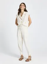 Pantalón jogger color crudo con estampado a cuadros, cintura con cordón ajustable, ribete elástico y minivolantes, bolsillos delanteros, detalles plisados y bajo con botones laterales.