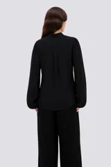Camisa de poliéster color marfil, de diseño holgado, con cuello alto lazada y mangas largas abullonadas.