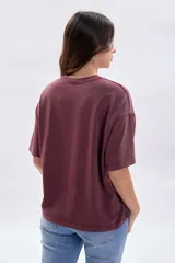Remera de manga corta con corte boxy, color bordó con efecto de teñido especial. Presenta una estampa frontal con el texto 'STOKHOLM FASHION ARCHIVE CREATIVE SPACE' en tono oscuro.