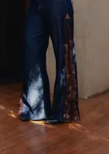 Pantalón de jean estilo wide leg, confeccionado en denim rígido de color azul oscuro. Presenta paneles laterales de encaje con diseño floral en tono rojizo y terminaciones deshilachadas en el ruedo.
