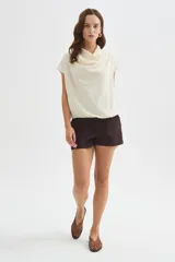 Blusa de poliéster color marfil, de corte holgado, sin mangas y con cuello buche drapeado.