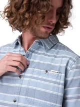 Camisa de manga corta Caterpillar, color celeste con diseño de rayas horizontales blancas y azules, corte regular y bolsillos en el pecho con botón y etiqueta con logo.