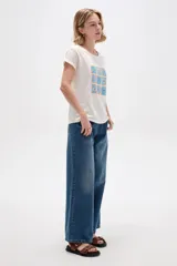 Remera de manga corta con cuello redondo y diseño holgado, en color blanco con estampado floral en tonos azules y destellos dorados.