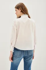 Camisa negra de algodón con cuello alto, cierre frontal de botones y detalles de encaje vertical y en los puños.