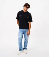 Remera de corte oversized confeccionada en mezcla de algodón y poliéster. Presenta cuello redondo, mangas cortas con hombros caídos y diseño estampado en la espalda con la frase 'LA THE START OF A NEW ERA' acompañada de estrellas amarillas.