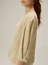 Blusa de algodón color marrón, con escote redondo, mangas tres cuartos con volumen sutil y costuras verticales decorativas en el frente.
