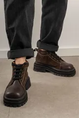 Borcegos de punta cuadrada con diseño acordonado, combinando paneles de cuero texturizado y gamuza en tonos marrones. Presentan una suela track gruesa de goma negra y cordones negros.