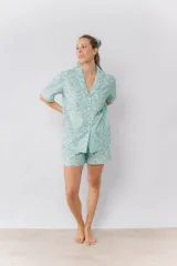 Pijama de algodón estampado con flores en tonos pastel sobre fondo verde menta. Incluye una camisa de manga corta abotonada con cuello solapa y un short con elástico en la cintura, ambos con detalles de picot en los bordes.