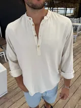 Camisola de lino color beige, con cuello mao y cierre frontal parcial con botones. Presenta mangas largas con puños doblados.