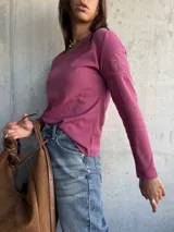 Remera de manga larga color rosa, con cuello redondo y detalle de bordado floral en el hombro izquierdo.