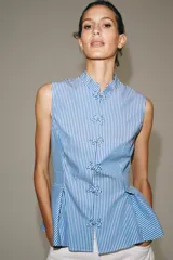 Camisa sin mangas de algodón con rayas verticales blancas y azules, cuello mao, bajo acabado en peplum y cierre frontal con alamares decorativos de nudo.