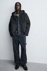 Cazadora tipo bomber de denim color negro con efecto lavado, corte boxy fit, cierre frontal de cremallera, capucha ajustable con cordón y bolsillos laterales de vivo.