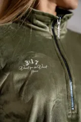 Buzo de plush color verde oliva, con cuello alto y cierre frontal parcial. Presenta mangas largas con puños elásticos y un pequeño bordado en el pecho.