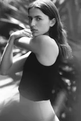 Top deportivo negro, corte cropped y ajustado, sin mangas y con cuello redondo. Presenta un detalle de nudo o torcido en el bajo frontal.