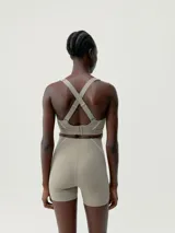 Top deportivo color beige con tirantes regulables cruzados en la espalda y cierre ajustable. Presenta una banda reflectante en el frente y copas extraíbles.