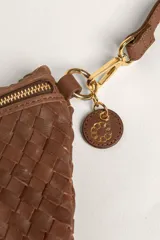 Bandolera de gamuza color marrón con diseño de media luna, decorada con tachas metálicas doradas distribuidas en el frente. Cuenta con cierre superior metálico y correa larga ajustable para llevar cruzada.