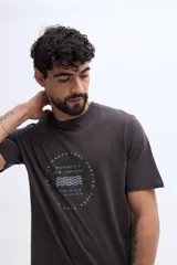 Remera Brooksfield de corte regular, color marrón, con cuello redondo, mangas cortas y estampa circular al frente en tonos claros con texto y líneas onduladas.