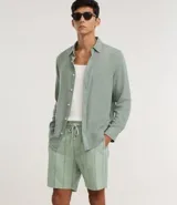 Bermuda recta de playa en color blanco roto, confeccionada en algodón texturizado con efecto de rayas verticales. Posee cintura elástica con cordón ajustable.