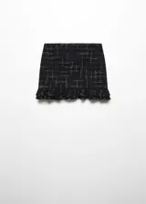 Minifalda negra de tweed con diseño a cuadros blancos, bajo asimétrico con volantes y cierre lateral con cremallera invisible.