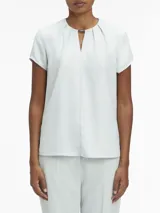 Blusa celeste de poliéster reciclado con cuello redondo, mangas cortas y cierre con cremallera en la espalda. Presenta una abertura en la parte delantera con una barra metálica decorativa.