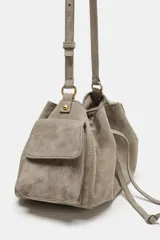 Mini bolso bandolera de piel color gris topo, con diseño fruncido, cierre mediante cordón ajustable y stopper, bolsillos exteriores laterales con solapa y botón imantado, y correa ajustable.