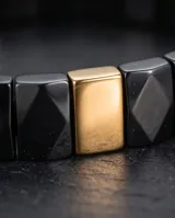 Pulsera elástica compuesta por eslabones de cerámica negra con acabado facetado y una pieza central rectangular con baño de oro.
