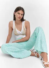 Pantalon de tiro medio con diseño acampanado, confeccionado en mezcla de lino y viscosa con estampado floral en tonos turquesa y blanco. Presenta bolsillos laterales, trabillas para cinturón, costuras decorativas frontales y cierre de cremallera con botón.