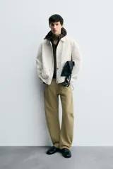 Cazadora de hombre, corte relaxed fit, color blanco hueso o crema, con acabado brillante. Presenta cuello solapa, manga larga, dos bolsillos de plastrón con solapa en la cadera y cierre frontal con botones a presión ocultos por una solapa.