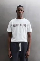 Camiseta de algodón gris melange con cuello redondo, mangas cortas y efecto lavado. Presenta un estampado de texto frontal en color oscuro con efecto desgastado.