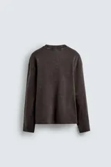 Camiseta de manga larga color marrón oscuro con efecto lavado (acid wash) y corte relajado. Presenta cuello redondo y aberturas laterales en el bajo.