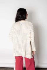 Poncho de punto color crudo con calce suelto y relajado. Confeccionado en tejido con lúrex que aporta un sutil brillo, presenta cuello en V, mangas anchas y textura acanalada.