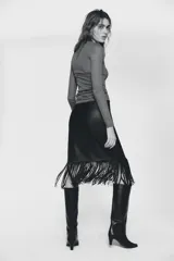 Falda midi de corte recto con diseño cruzado en el delantero y bajo terminado en flecos largos. Confeccionada en material efecto piel con cierre lateral mediante cremallera oculta.