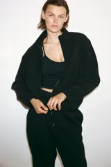 Campera deportiva de sherpa cálida y suave, color negro, con cuello elevado, cierre frontal y bolsillos laterales. Cuenta con corte holgado y elásticos en puños y bajo.