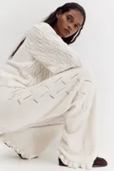 Pantalón de punto suave color beige, de tiro alto con cintura elástica, perneras rectas, secciones laterales con diseño pointelle y detalle de volados en el bajo.
