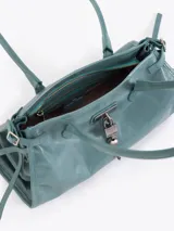 Cartera de hombro confeccionada en cuero vacuno color azul petróleo con acabado brillante. Presenta un diseño rectangular con herraje metálico tipo candado y dijes colgantes en el frente, además de correas laterales ajustables con tiras decorativas.