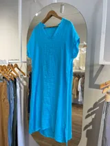 Vestido midi de lino color beige, corte recto, con escote en V y mangas cortas. Presenta aberturas laterales en el ruedo.