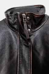 Chaqueta bomber de cuero negro con cuello alto, manga larga con cremalleras metálicas, bolsillos de plastrón con solapa y botón en delantero, bajo acabado en elástico y cierre frontal con cremallera y botones a presión ocultos por solapa.