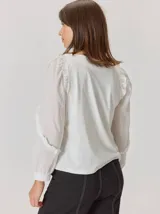 Camisa de color marrón con diseño combinado, presentando mangas abullonadas con volados en los hombros y cuerpo de algodón. Combina una textura de tela de camisa en mangas y delantero con una espalda de tejido elástico.